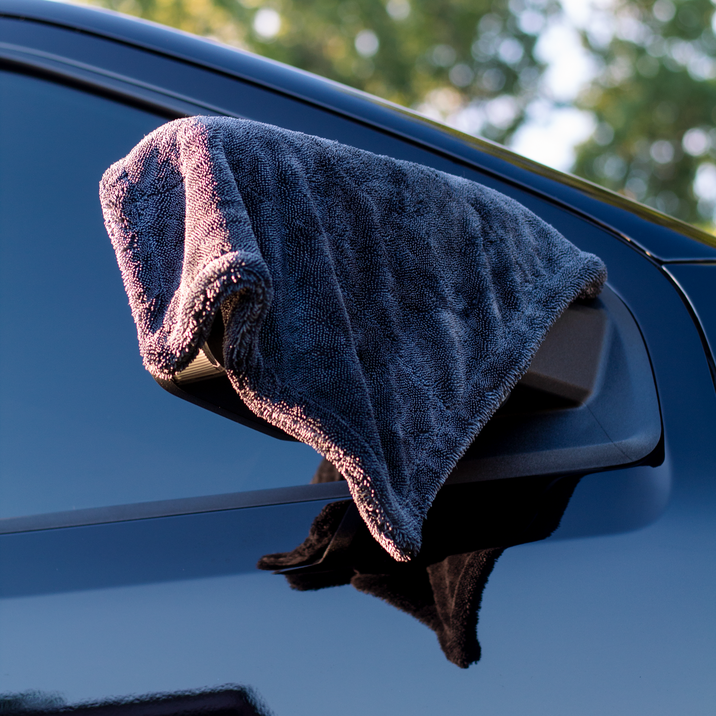 Gray microfiber towel draped over a car's side mirror with a blurred natural background