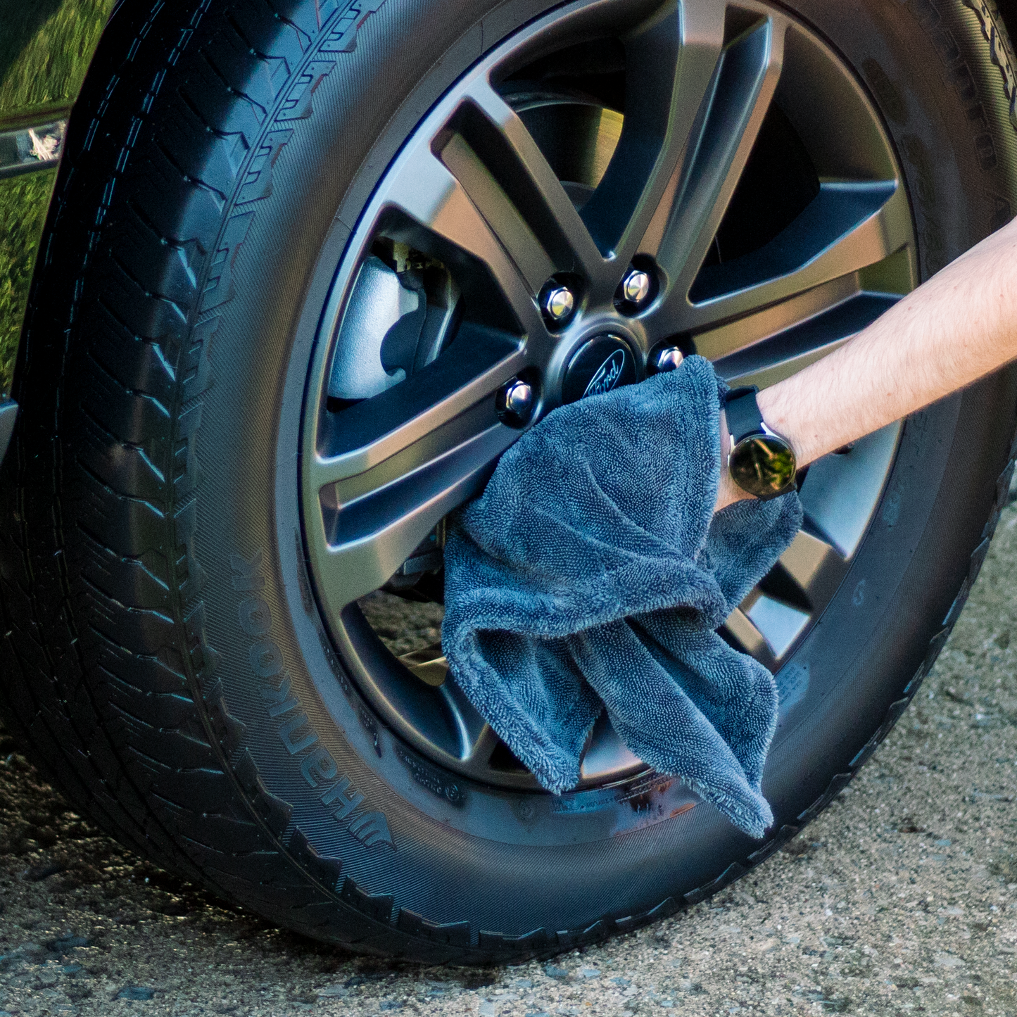 Person cleaning a car wheel with a microfiber towel