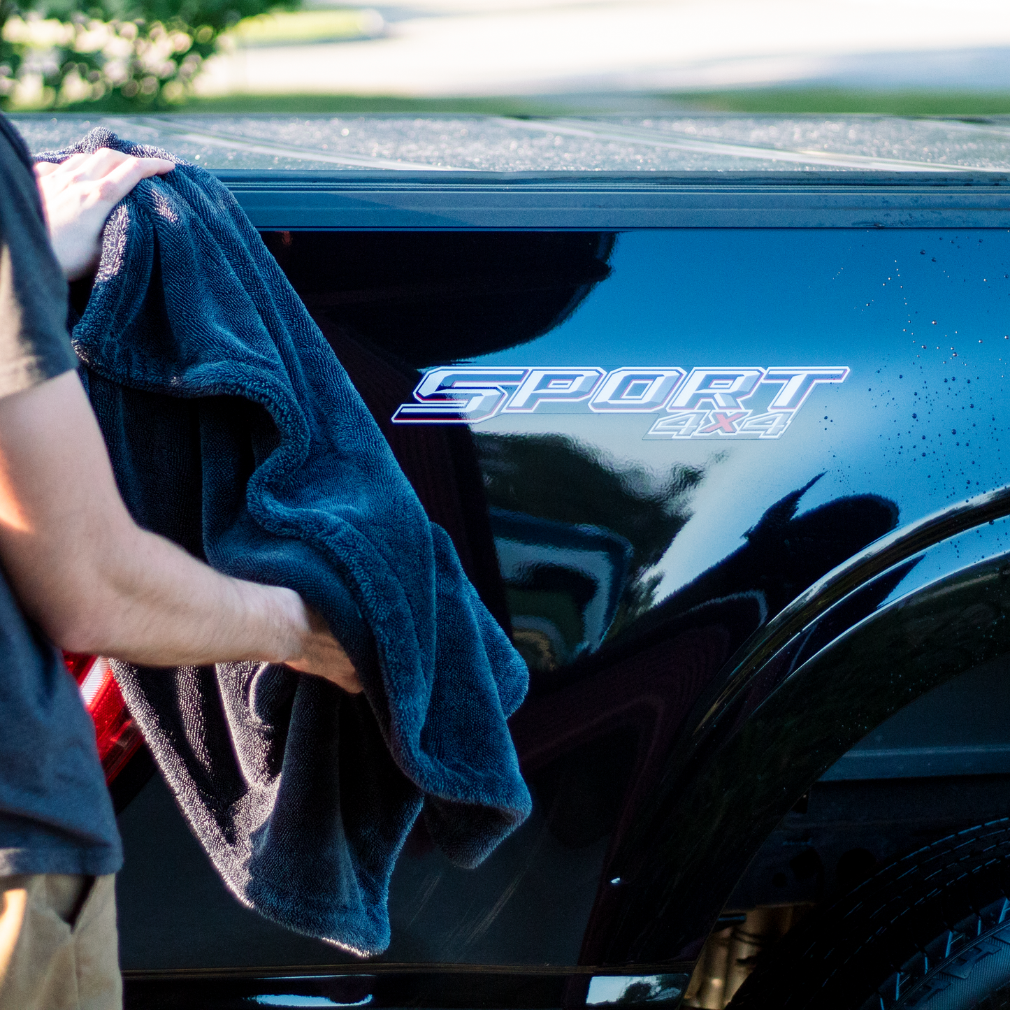 Person cleaning a black car with 'NightGloss' logo using a black towel.
