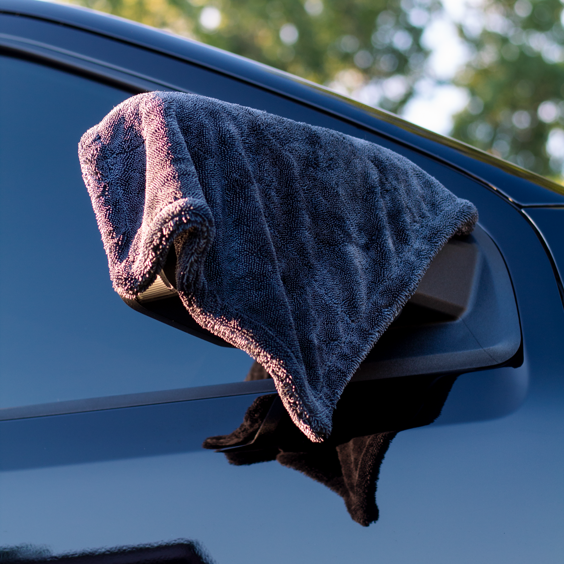 Gray microfiber towel draped over a car's side mirror with a blurred natural background