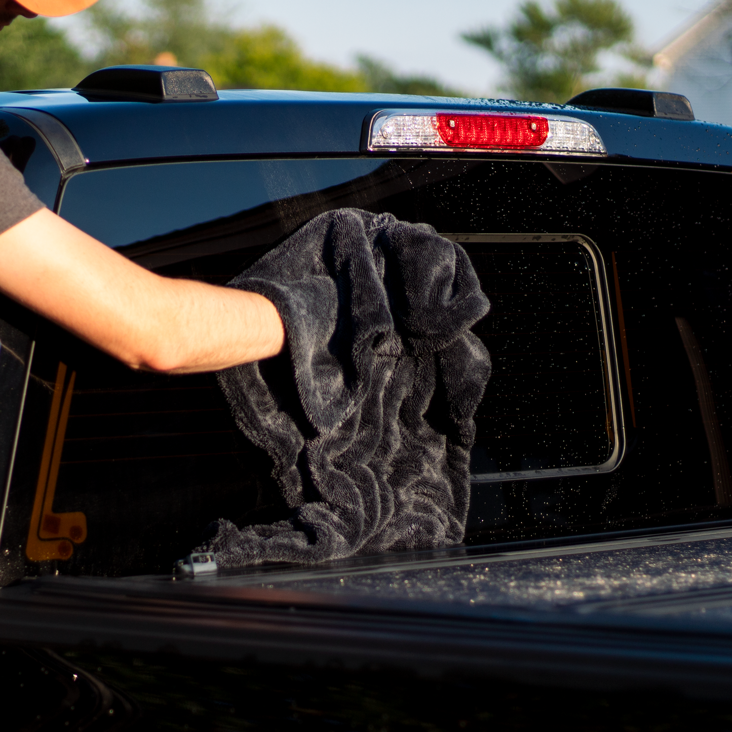 Person cleaning a car window with a black towel outdoors