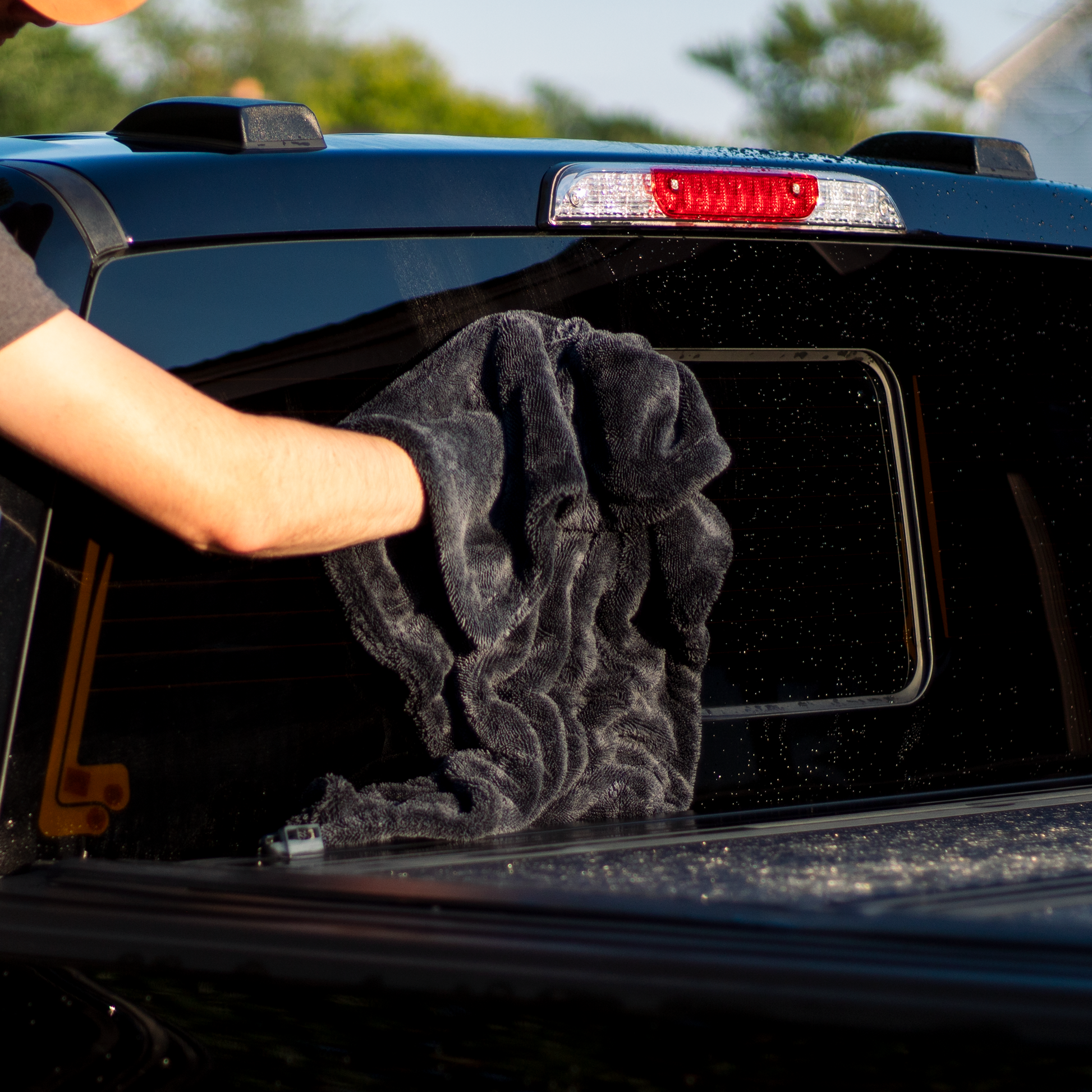 Person cleaning a car window with a black towel outdoors